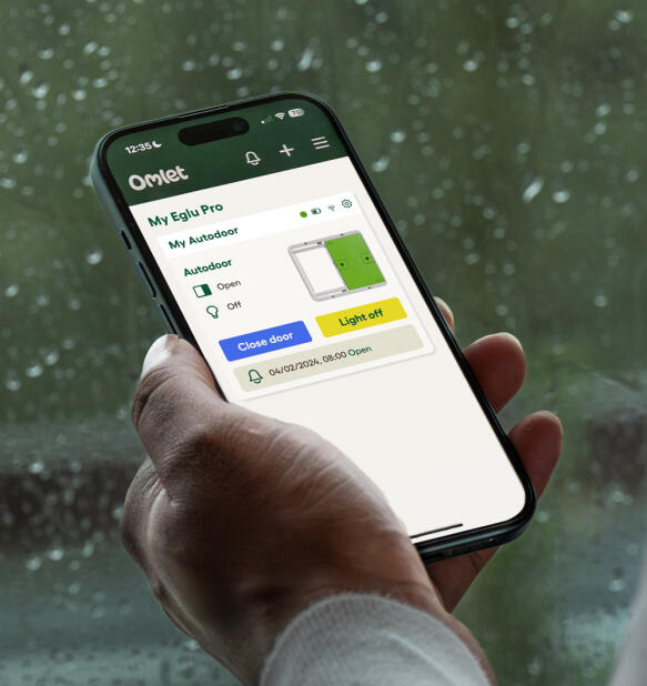 Hand som håller i en telefon med Omlet smart Autodoor app öppen
